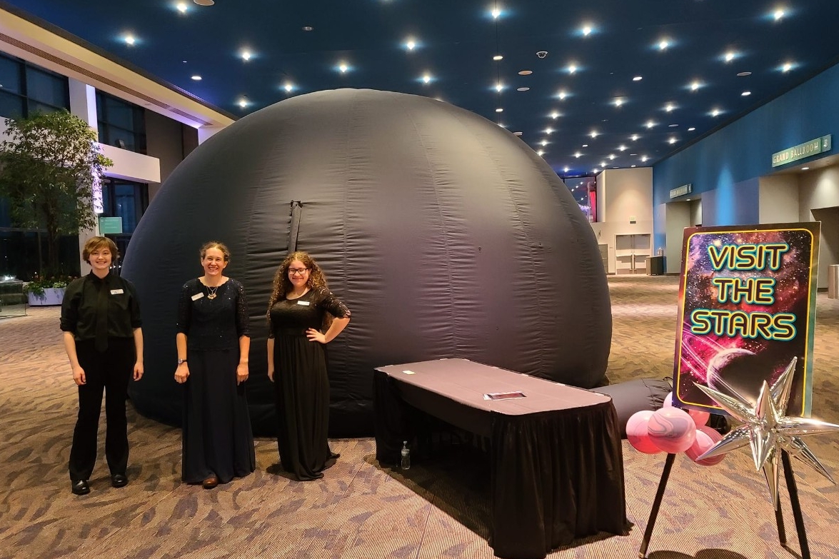 NKU Haile Planetarium Roaming Dome Planetarium staff smile in front of the Roaming Dome at a private event in a convention center.