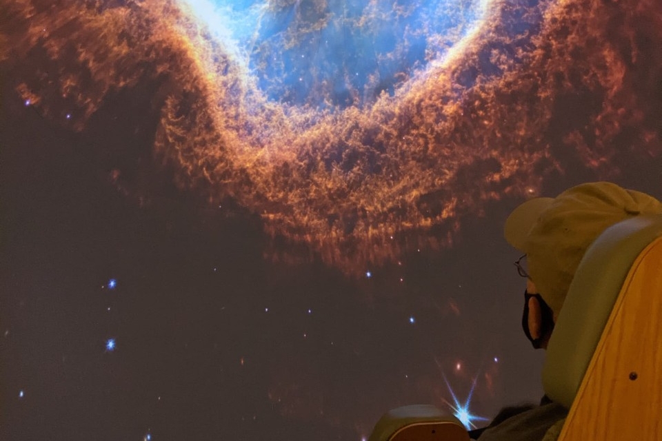 A planetarium visitor gazes at a galaxy filled screen.