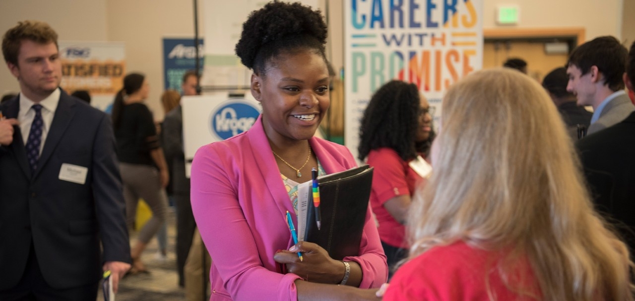 Student and employer at a career fair shaking hands and talking