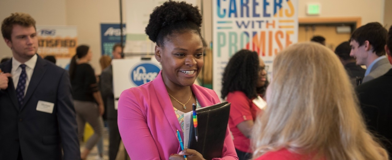 Student and employer at a career fair shaking hands and talking