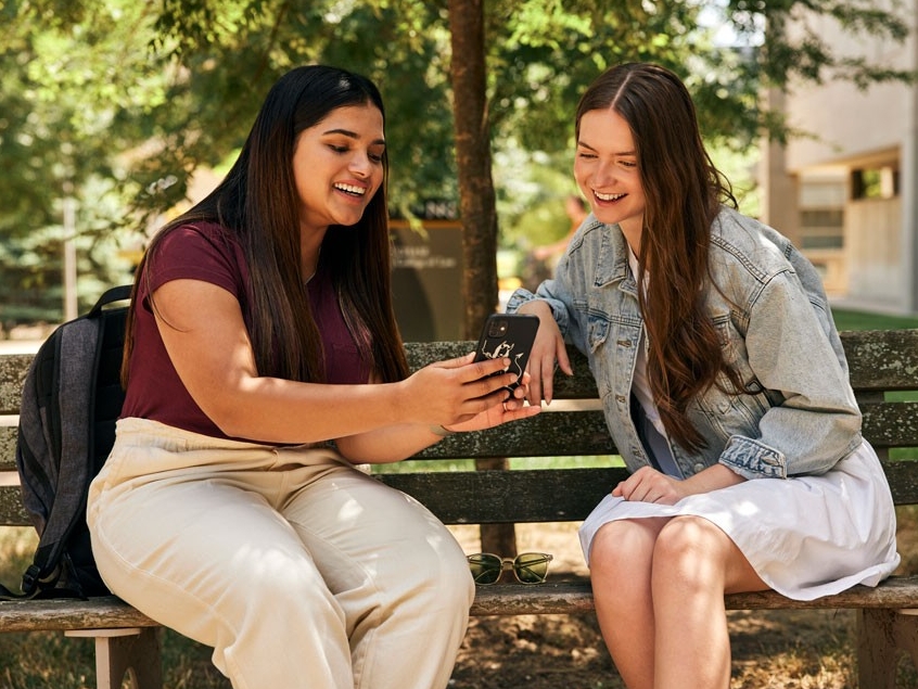 Students talking and laughing at a park bench on campus