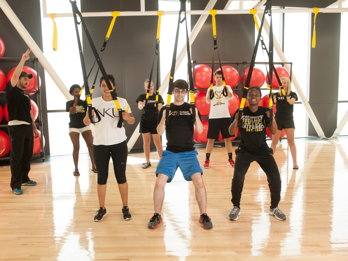 Seven students participating in a fitness class inside a campus rec gym.