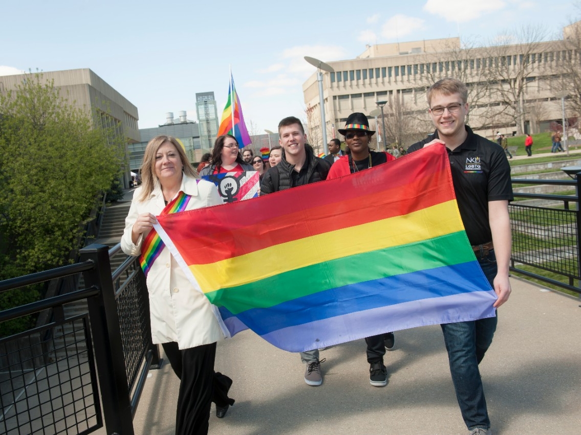Students holding up the LGBTQA+ flag in a Pride Parade.