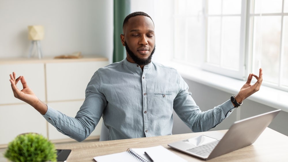 Peaceful African Businessman Meditating Sitting At Workplace Relaxing In Office Man sitting at a desk meditating
