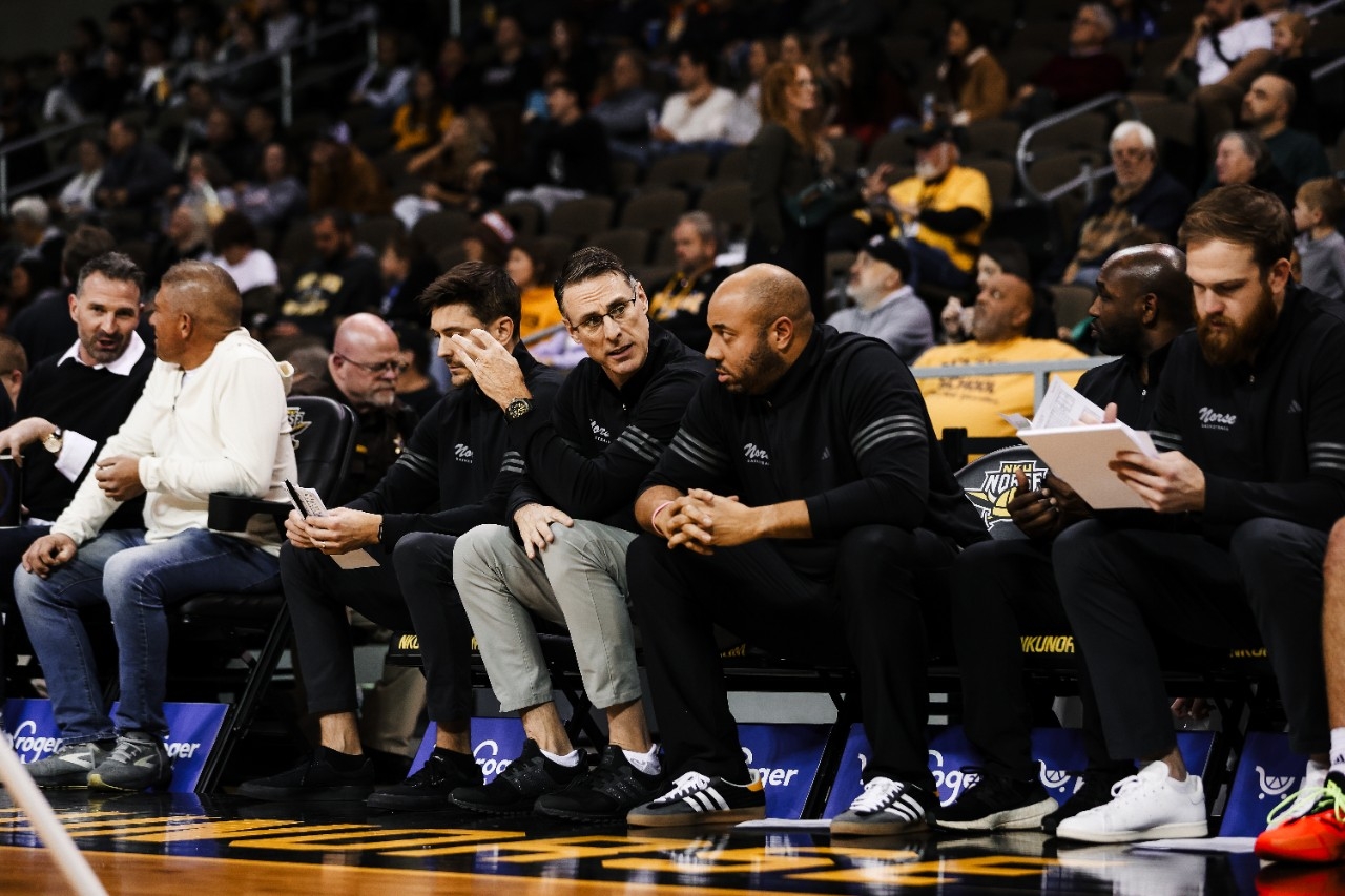 NKU men's basketball head coach Darrin Horn sits with coaches on the bench at an NKU home game.