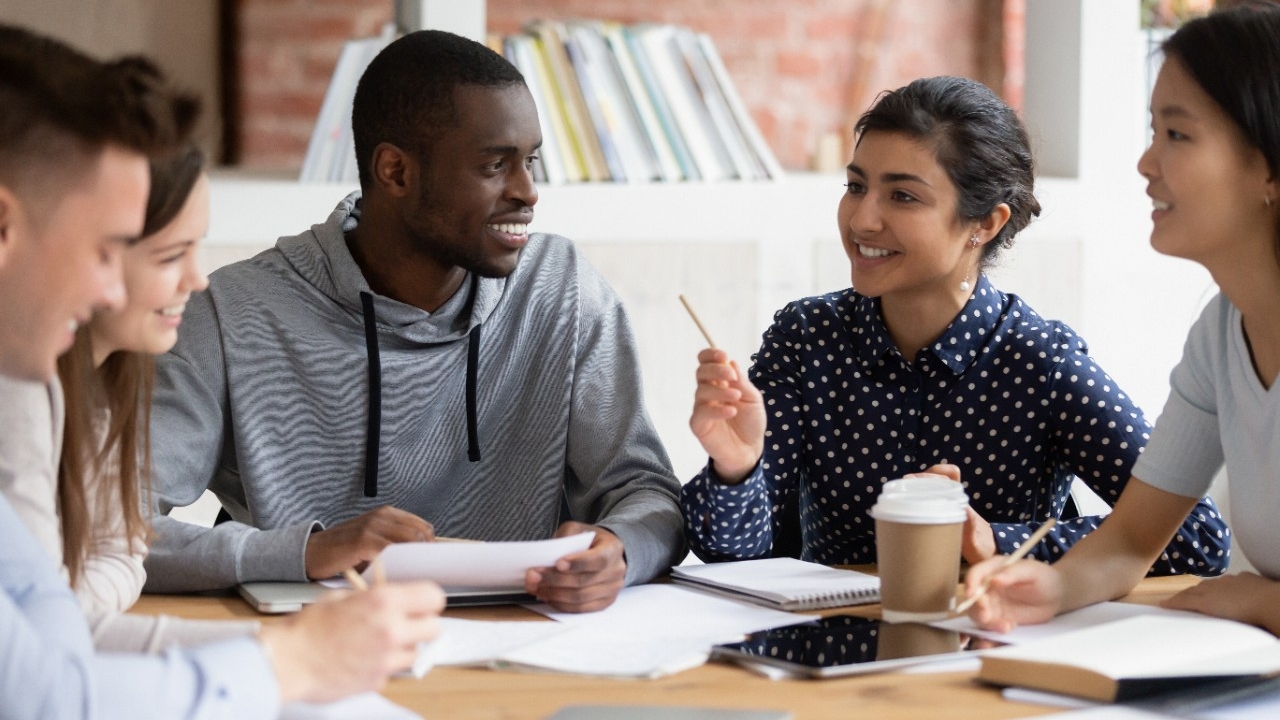 Students talk at a table with books and coffee